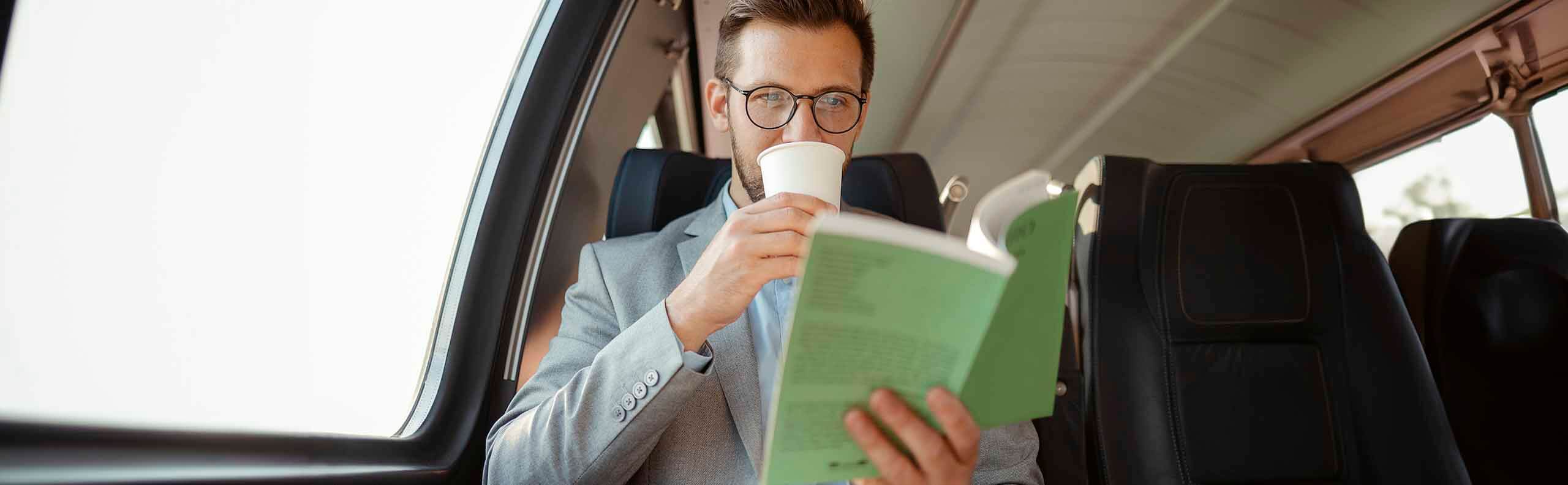 man reading a business book while drinking coffee on public transport