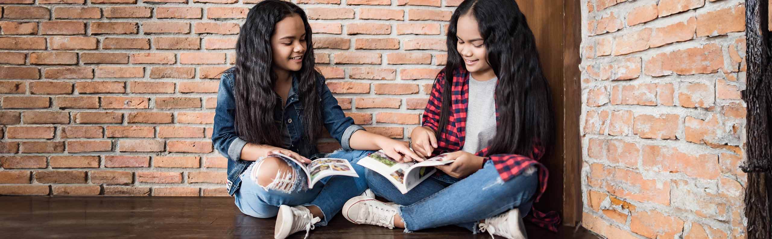 Two girls reading graphic novels together and smiling