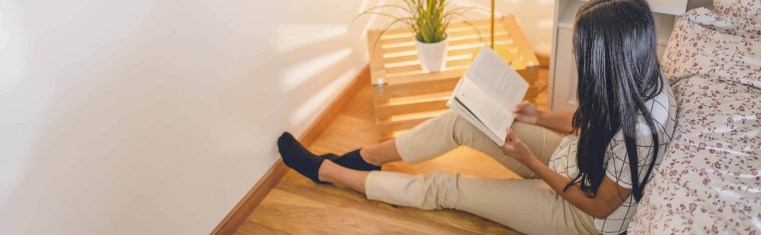 Woman sitting on the floor by her bed reading poetry